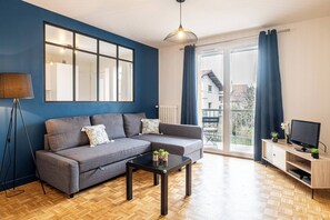 A modern living room with a sofa, a coffee table, a TV stand, and a large window with curtains.