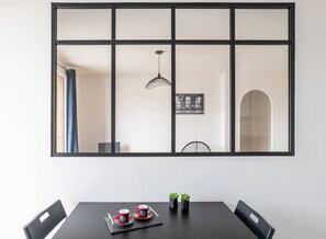 A dining area with a table, chairs, a black tablecloth, two red cups, two small potted plants, and a pendant light.
