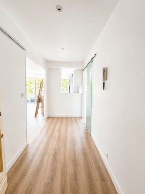 A spacious hallway with wooden flooring, a sliding glass door, and a ladder in the background.