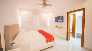 A bedroom with a bed, a ceiling fan, a TV on the wall, and a wooden door leading to another room. - First Class 4br King Size Villa In Sosua Town! (Sosúa)