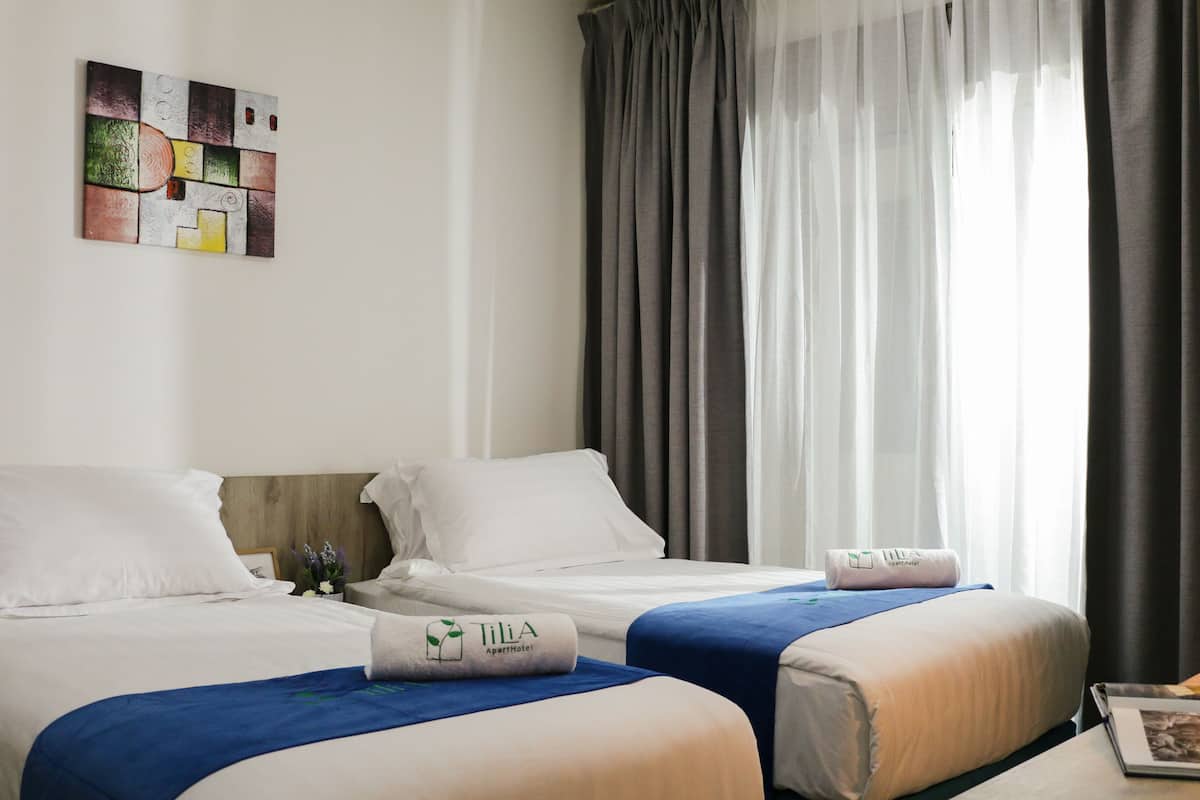 Quarto de hotel com duas camas, cabeceira de madeira, uma obra de arte na parede e uma janela com cortinas.