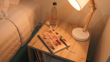 Una mesita de noche de madera con una lámpara, una botella de agua y un cuaderno de bocetos.