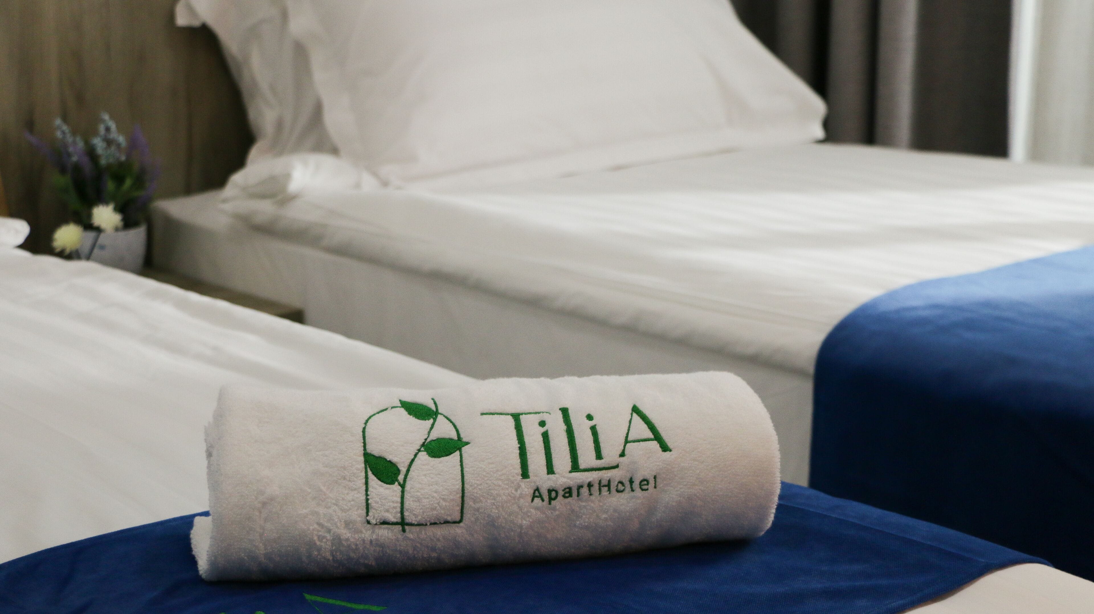 Un lit bien fait, avec une serviette ornée du logo de l’hôtel Tilla Apartment.