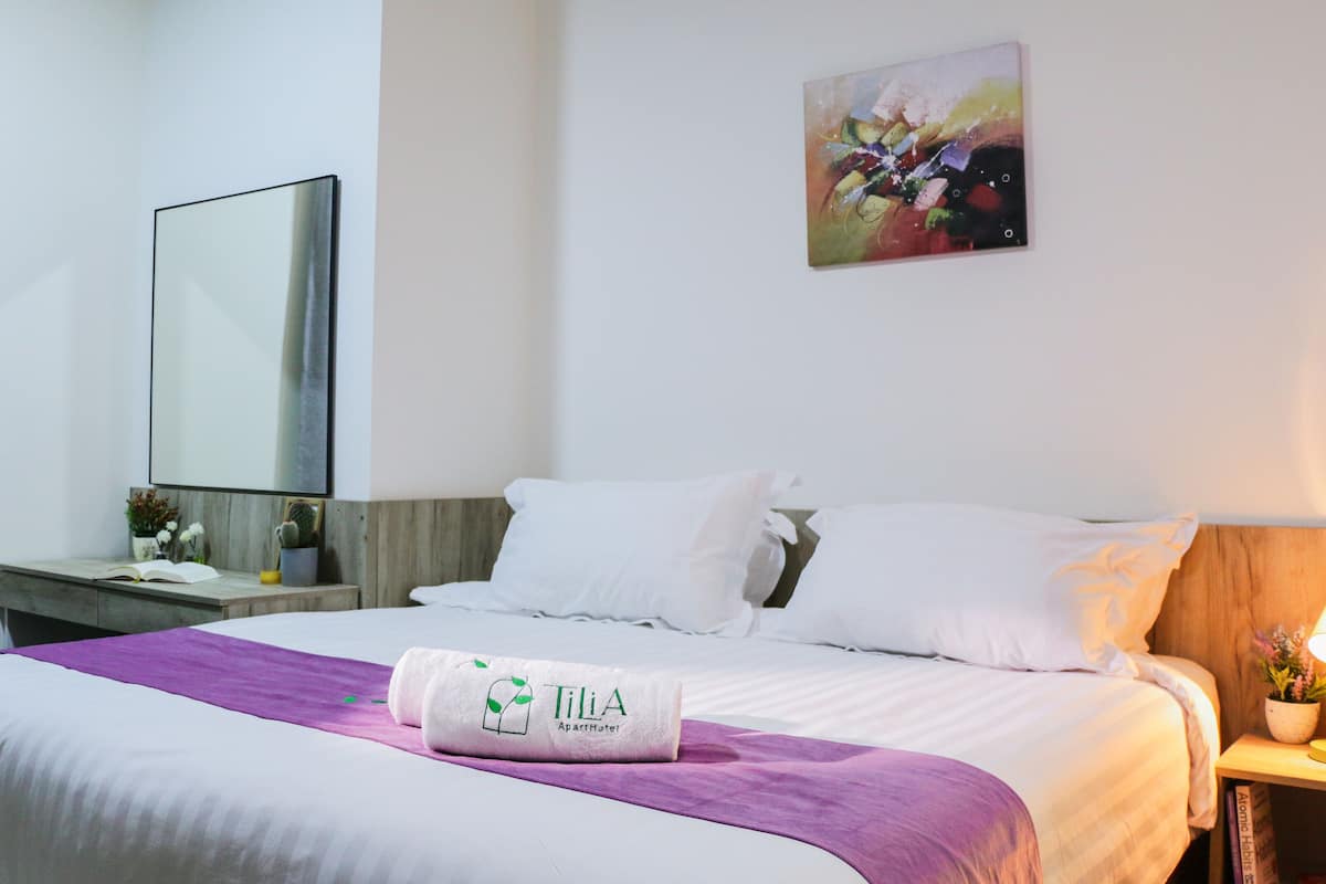Quarto de hotel com uma cama, mesa de cabeceira com abajur, espelho e um quadro na parede.