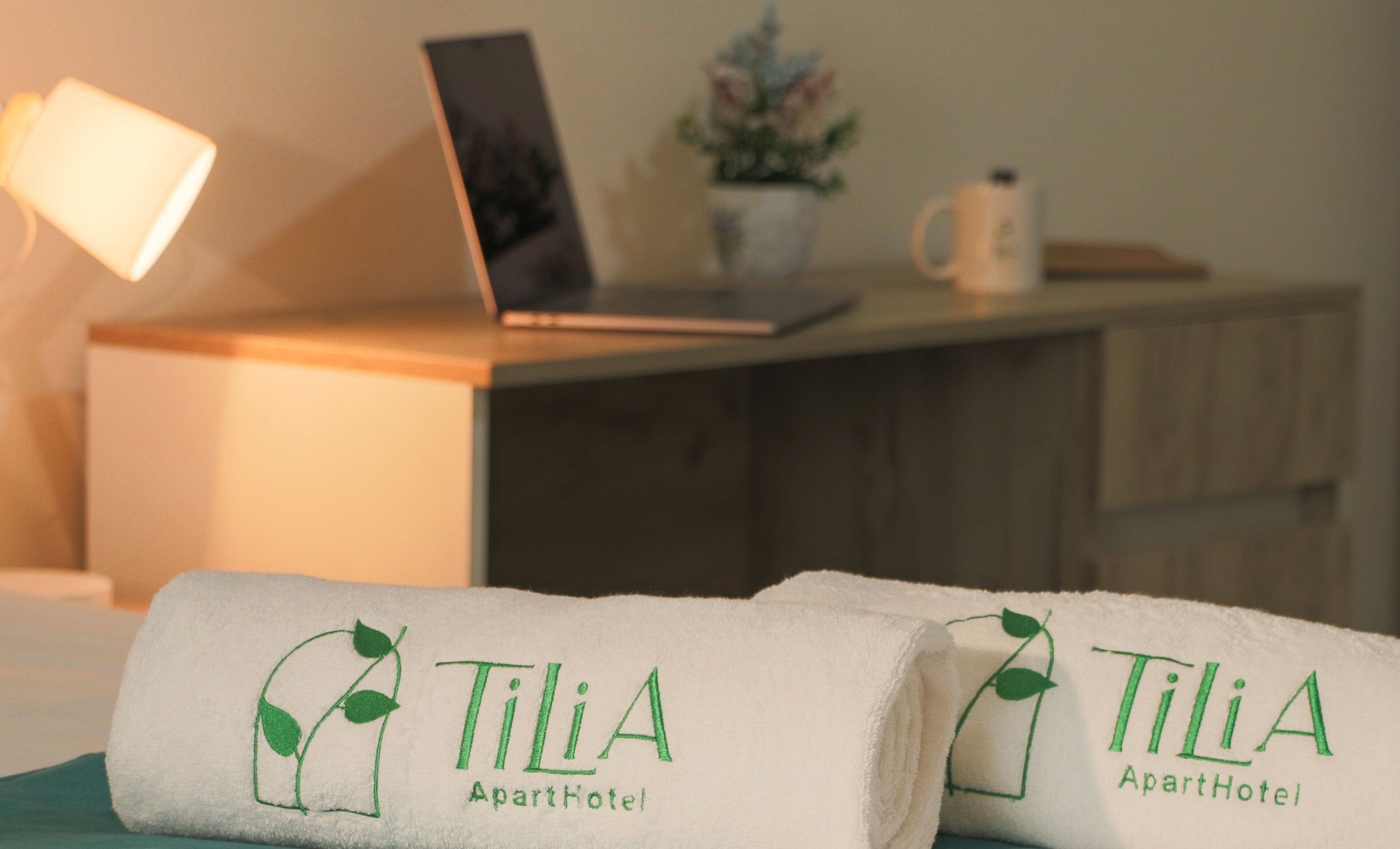 Two towels with the Tilia Apartment Hotel logo on a bed.