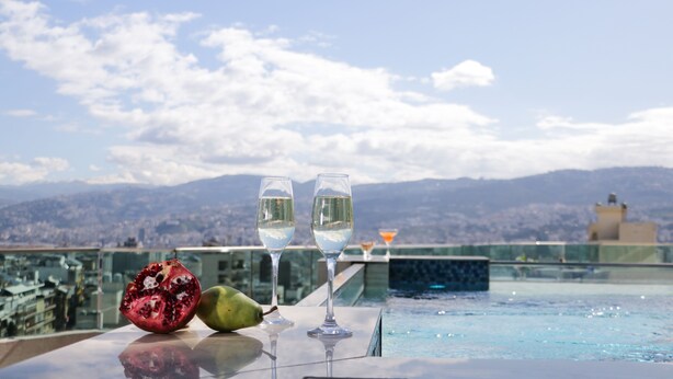 Una mesa con dos copas de vino y una granada en un balcón con vistas a una ciudad y montañas.