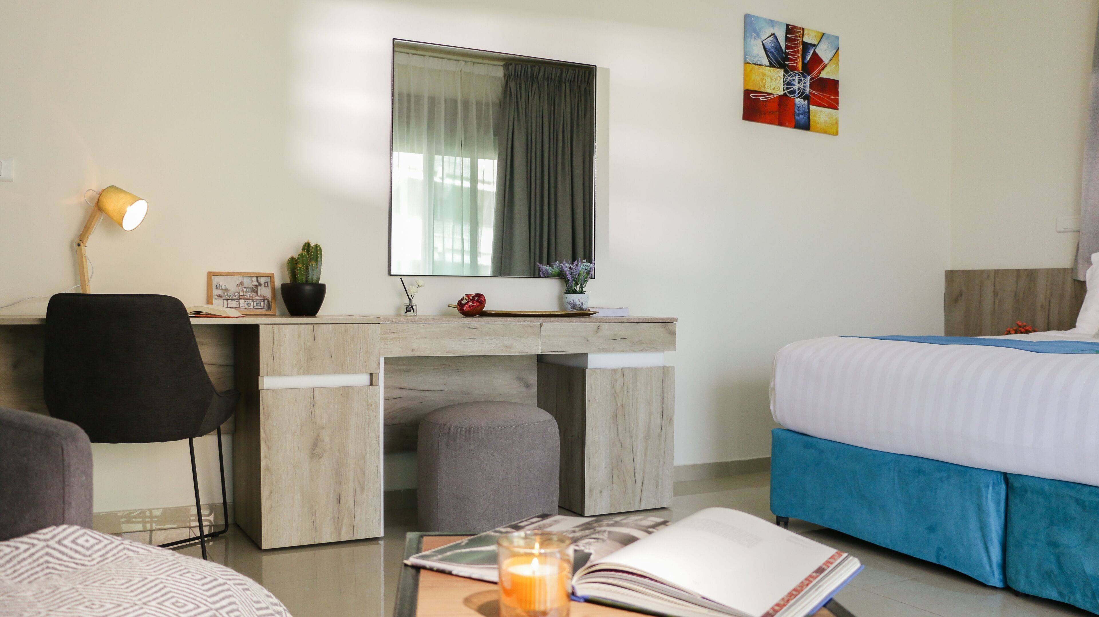 A hotel room with a desk, chair, bed, and a painting on the wall.