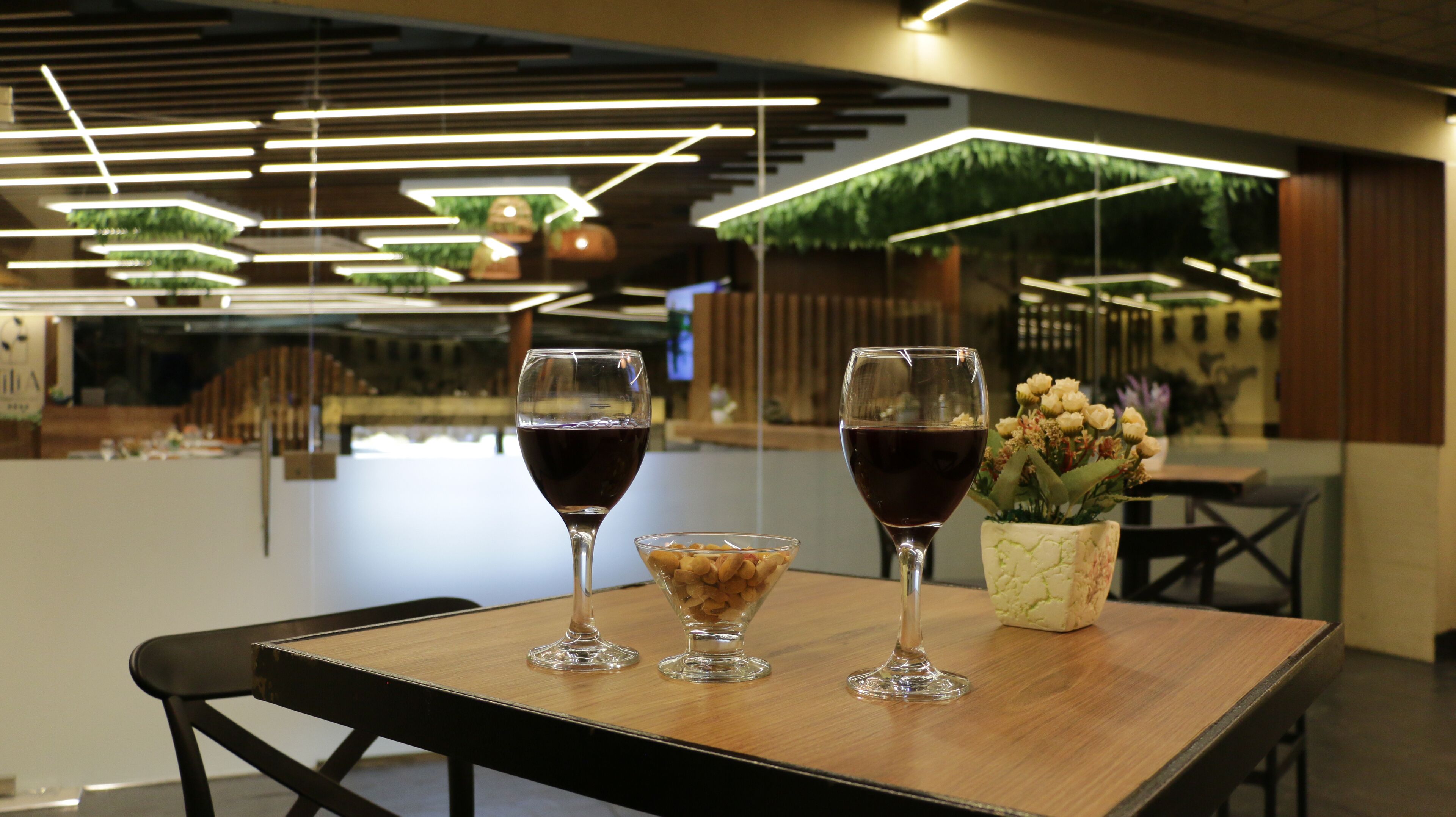 A table with two wine glasses and a bowl of nuts, set in a modern restaurant with a wooden table and black chairs.