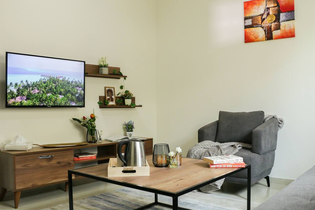 Uma sala de estar moderna com uma TV de tela plana, um sofá cinza, uma mesa de centro de madeira e uma estante.