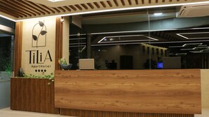 Mostrador de recepción en el Hotel Apartamentos Tilia, con un diseño moderno, que incluye un mostrador de madera, un letrero en la pared y una zona de recepción con una computadora y una planta.