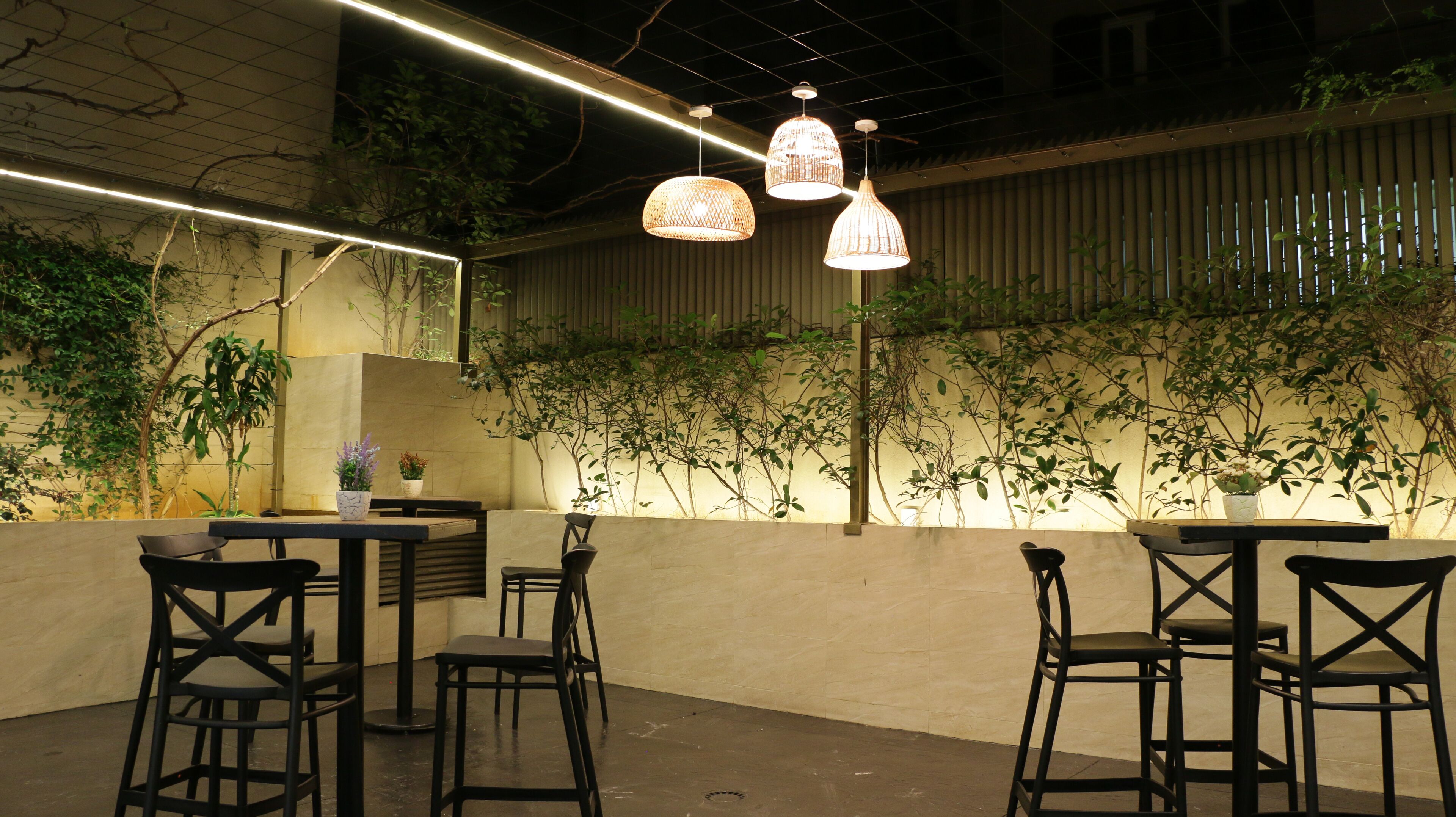 An outdoor seating area with tables and chairs, surrounded by plants and a bamboo wall.