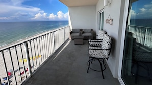 Een balkon met uitzicht op de oceaan, een bank, een gestreept fauteuil en een welkomstbord.