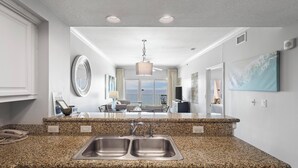 Een keuken met granieten aanrechtbladen, dubbele spoelbakken en uitzicht op de woonkamer met een balkon.