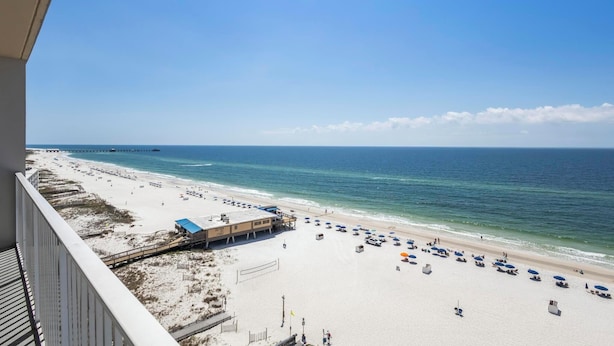 Uitzicht op een strand vanaf een balkon, met een heldere lucht, een zandstrand en een pier in de verte.