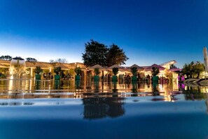 A nighttime outdoor area with a reflective pool, seating areas, and various structures. - Novum by the sea (Olimp)