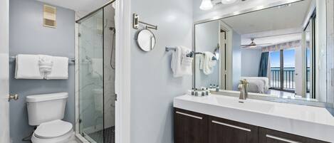 Un baño moderno con ducha envuelta en vidrio, inodoro blanco, espejo grande y tocador con armarios de madera oscura.