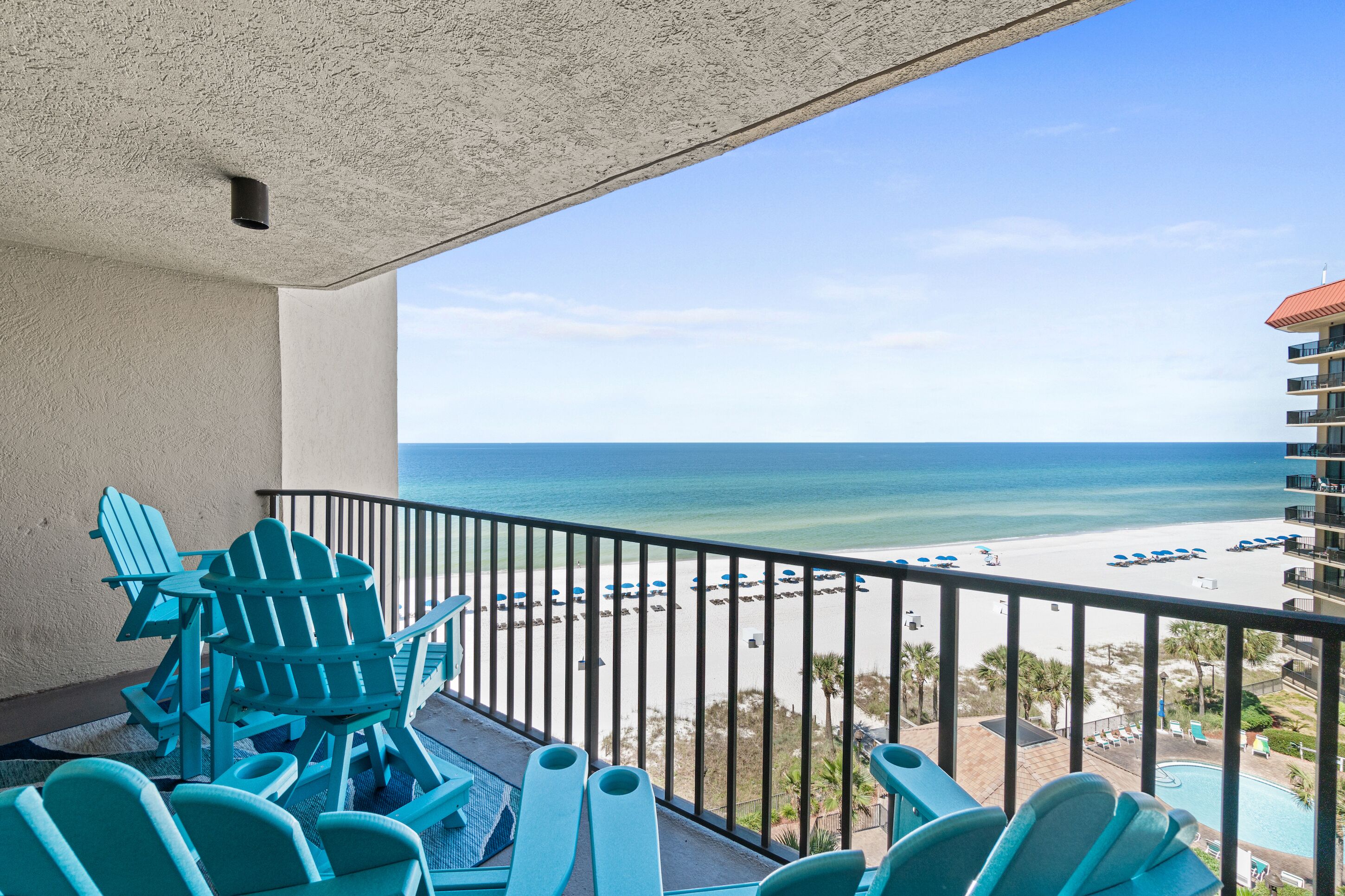 Ein Balkon mit blauen Adirondack-Stühlen und Blick auf Strand und Meer.