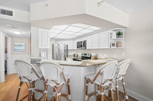 A modern kitchen with white cabinetry, a central island with bar stools, stainless steel appliances, and a skylight.