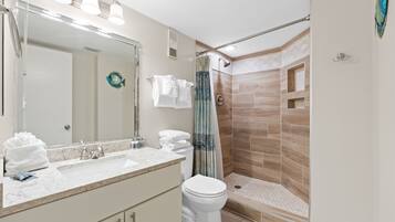 A modern bathroom with a large mirror, a sink, a toilet, and a walk-in shower with a glass door.