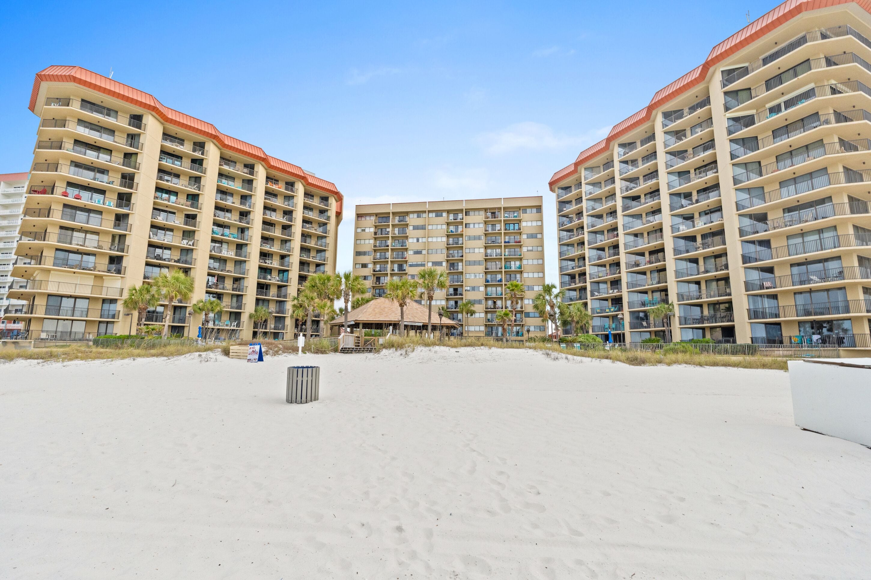 Ein Hotel direkt am Strand mit mehreren Etagen, Balkonen und einem zentralen Gebäude mit rotem Dach.