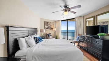 A bedroom with a large bed, a ceiling fan, a TV, and a view of the ocean.