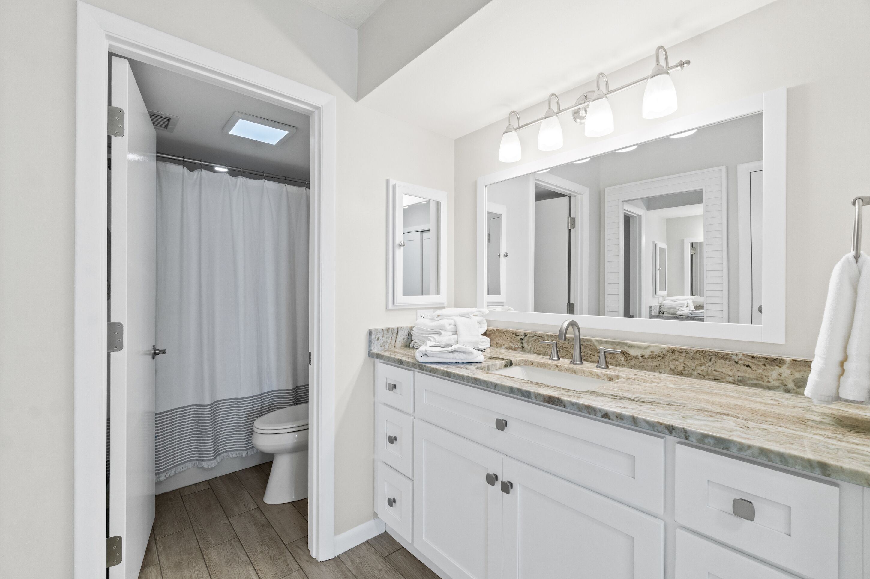 Un baño moderno con tocador blanco, un espejo grande y zona de ducha.