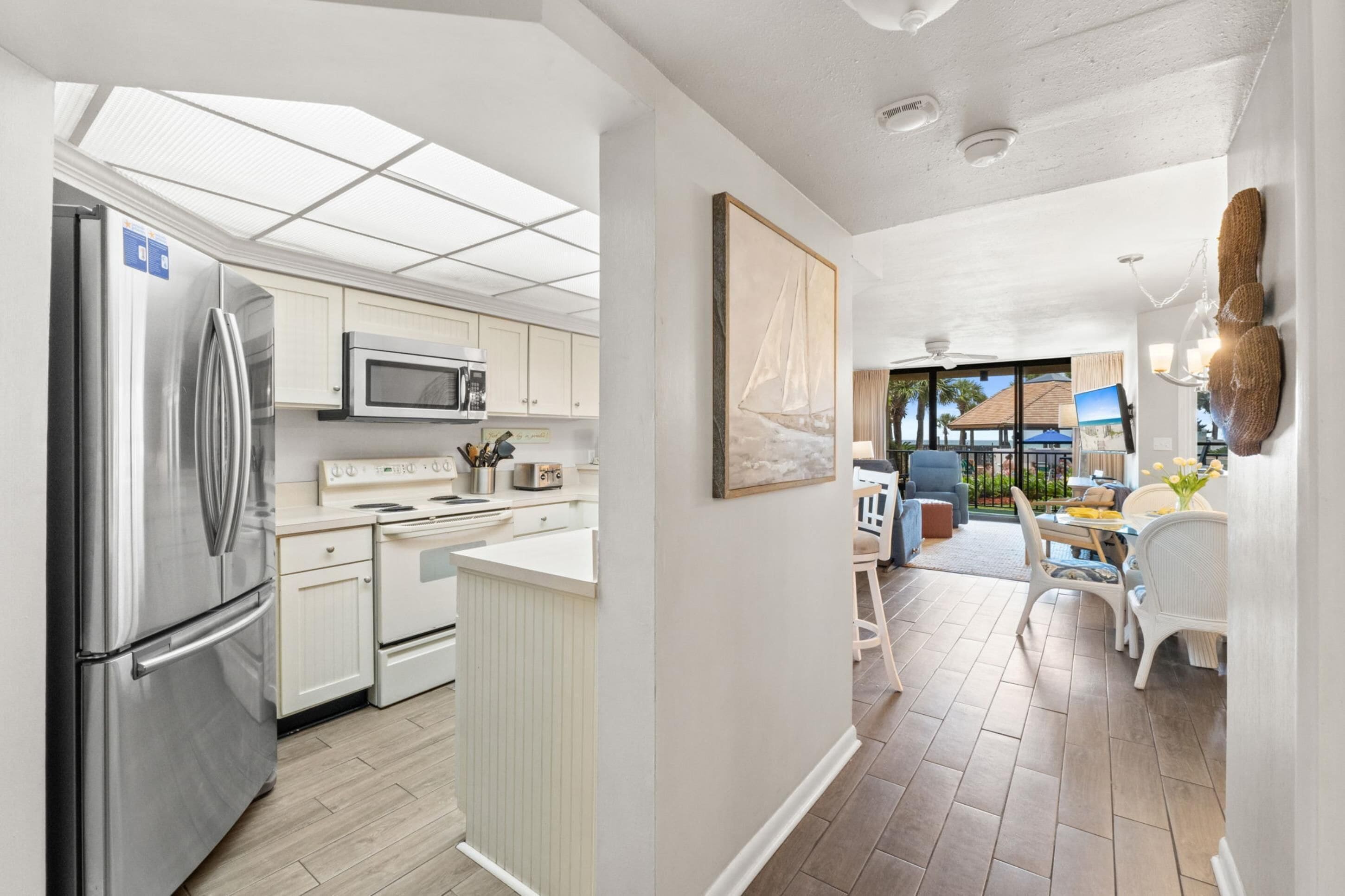 Una cocina moderna con electrodomésticos de acero inoxidable, un comedor con mobiliario blanco y vistas al exterior.