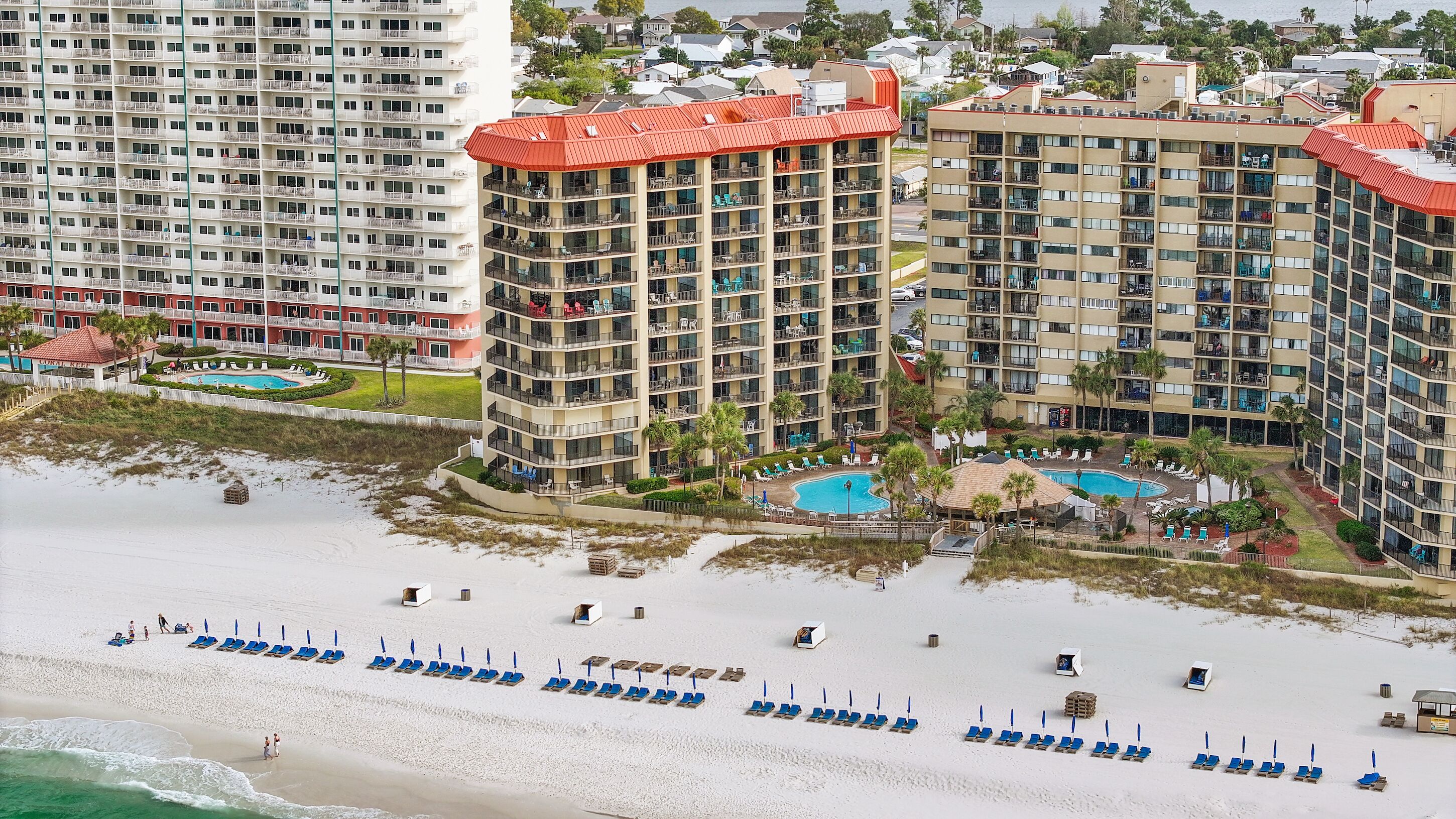 A high-rise hotel with multiple balconies, a pool area, and a beach with sun loungers.