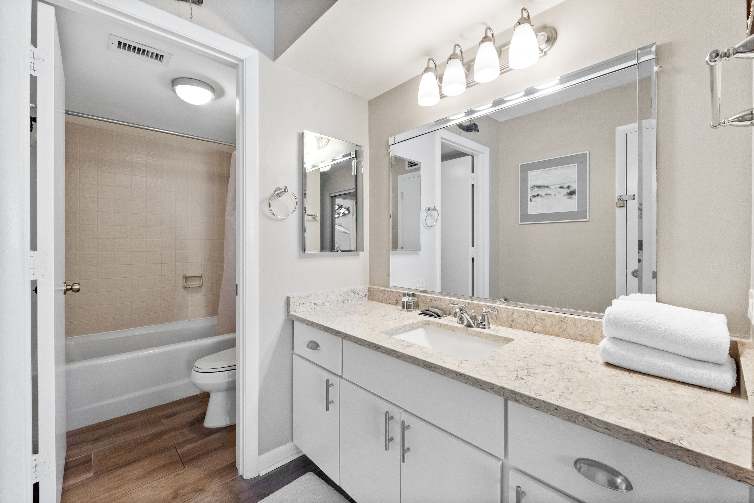 A modern bathroom with a bathtub, toilet, vanity with a sink, and a large mirror.