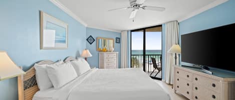 A hotel room with a large bed, a television, a ceiling fan, a balcony with a view, and a dresser.