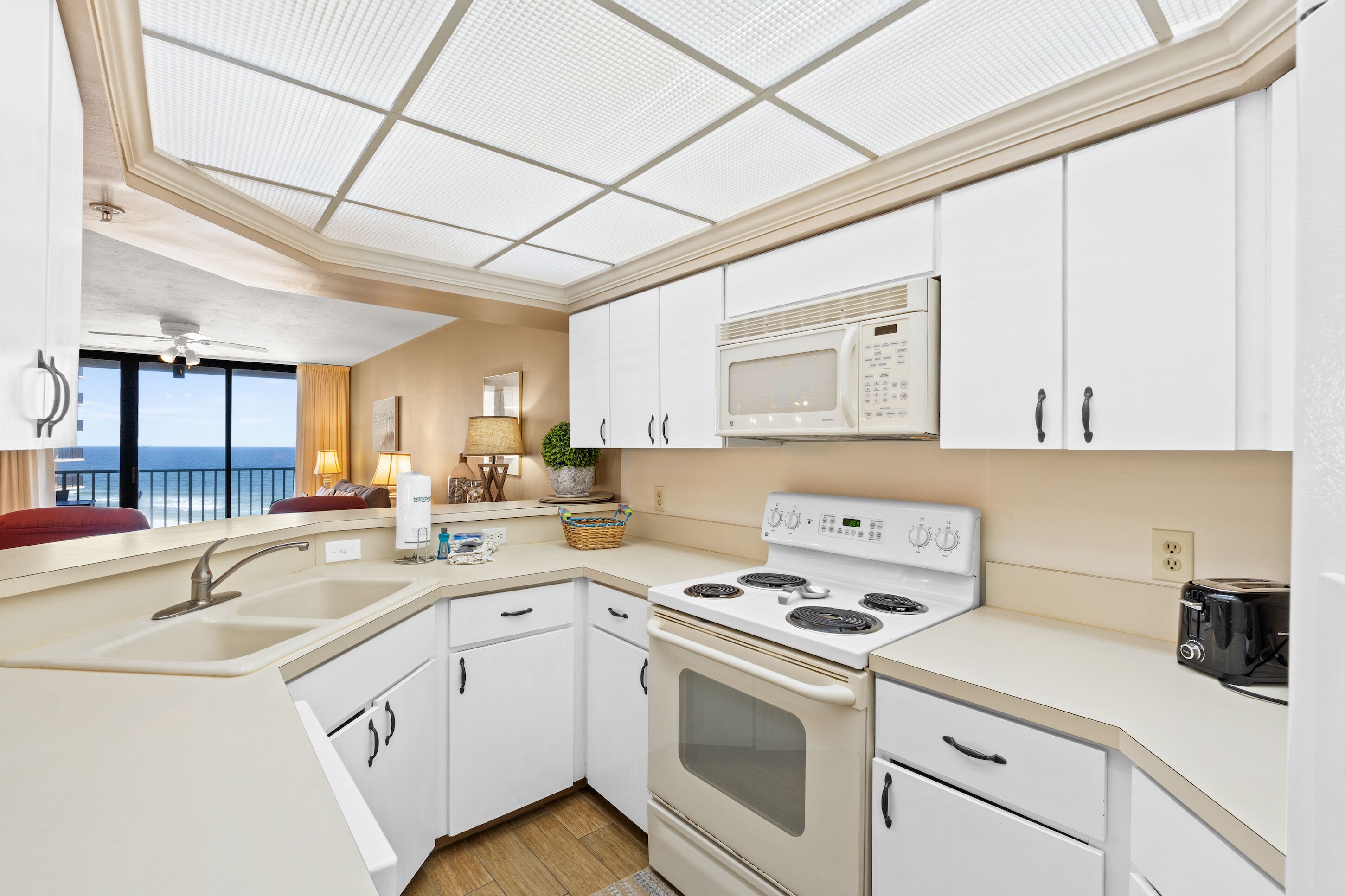 Een moderne keuken met witte kastjes, een ingebouwde magnetron, fornuis en een groot raam met uitzicht op de oceaan.