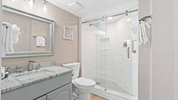 A bathroom with a large mirror, a sink, a toilet, and a glass-enclosed shower.