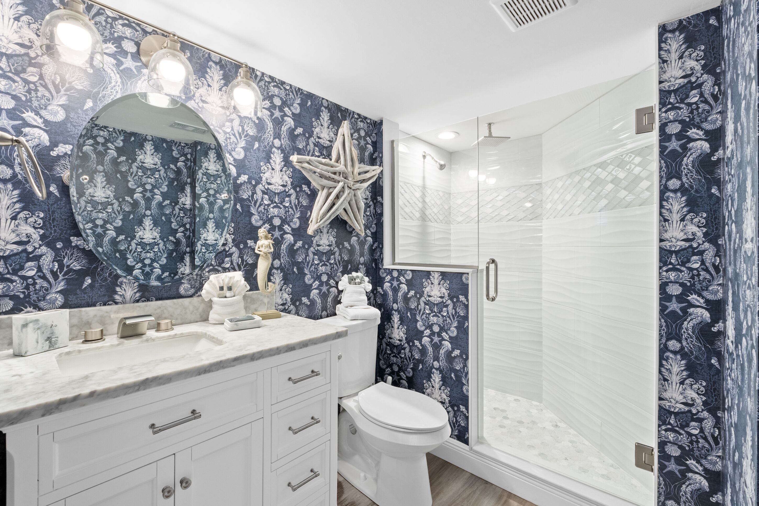 A bathroom with a large mirror, a starfish decoration, a toilet, and a glass-enclosed shower.