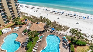 A resort with a large pool area, a beach with umbrellas, and a view of the ocean.