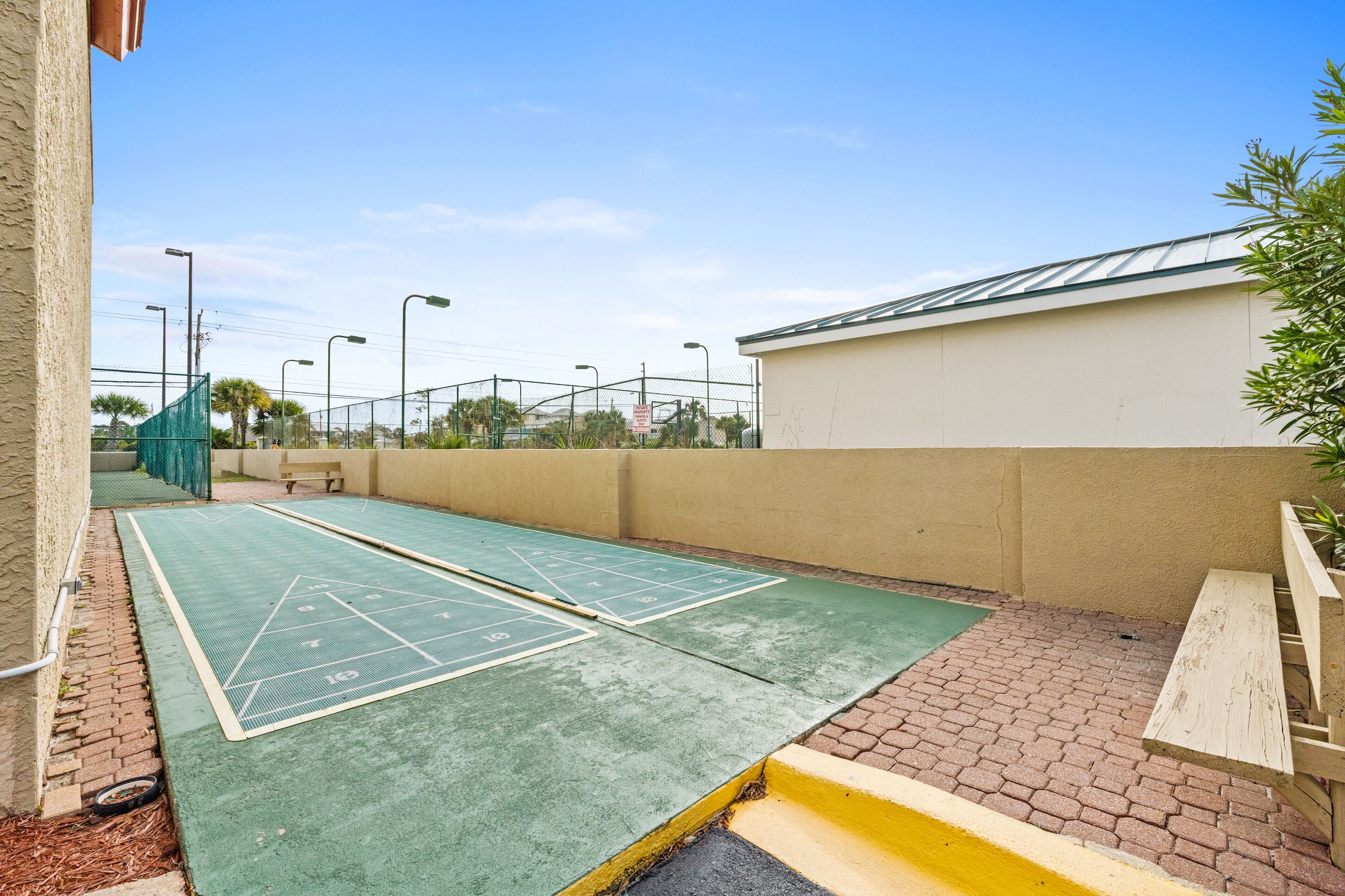A green shuffleboard court adjacent to a building with a beige wall and a wooden bench.