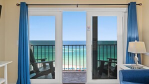 A room with a view of the ocean, a balcony with chairs, and a table.