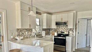 Une cuisine moderne avec des meubles blancs, un îlot central doté de tabourets, une cuisinière en acier inoxydable et un pare-feu orné d’un motif en forme de coquillage.