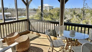 Un espace extérieur abrité, aménagé avec des meubles en osier, une table en verre et offrant une vue sur une maison et des arbres.