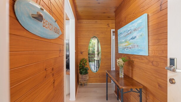Un pasillo de madera con un cartel que dice 'BEACH HOUSE', un espejo, un cuadro, un banco y una planta en maceta.