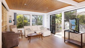 Amplia sala de estar con techo de madera, ventanas grandes, sofá, mesa de centro y televisor.