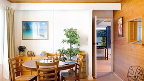 Un comedor con una mesa y sillas de madera, una planta en maceta y un cuadro en la pared.