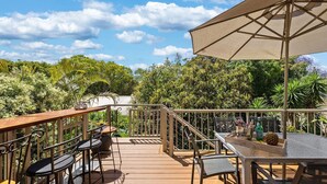 Una terraza al aire libre con muebles de madera, barandilla de metal y un paraguas grande.