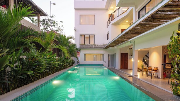 A swimming pool with tiled flooring, surrounded by lush greenery and a modern building with balconies and a dining area. - Serenity Suites d'Angkor (Siem Reap)