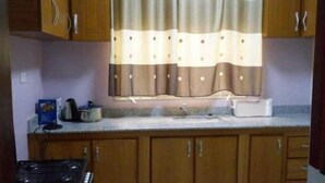 Une cuisine avec des meubles de rangement en bois, un plan de travail et une fenêtre ornée d’un rideau à rayures.