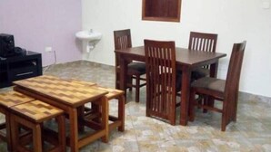 Un coin repas avec une table et des chaises en bois, un petit évier et un téléviseur posé sur un meuble.