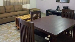 Un salon comprenant un canapé, une table à manger en bois avec des chaises, un téléviseur et une fenêtre avec des rideaux.