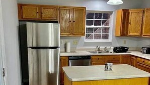 A kitchen with wooden cabinets, a stainless steel refrigerator, a dishwasher, and a window above the sink. - The Winchester (Winchester)