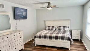 A bedroom with a bed, a dresser, a nightstand, a ceiling fan, and a TV mounted on the wall. - The Winchester (Winchester)