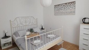 Quarto com cama, mesas de cabeceira, penteadeira, luminária pendente e uma obra de arte na parede.