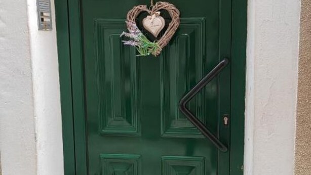 Uma porta verde com um ornamento em formato de coração e uma maçaneta preta.